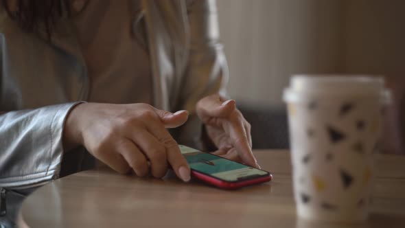 Woman Sits Indoors Puts Mobile Phone on the Table Takes a Paper Cup of Coffee