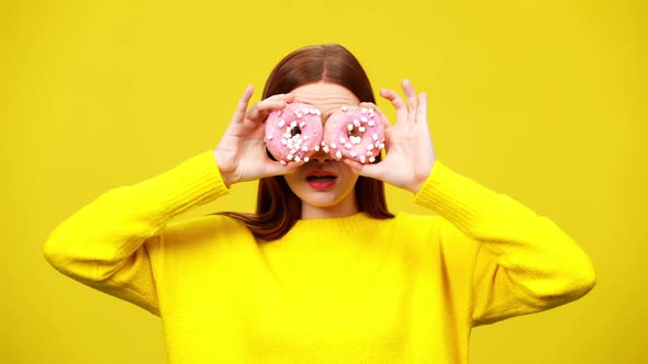 Middle Shot of Charming Joyful Redhead Woman Covering Eyes with Pink Donuts in Slow Motion alt