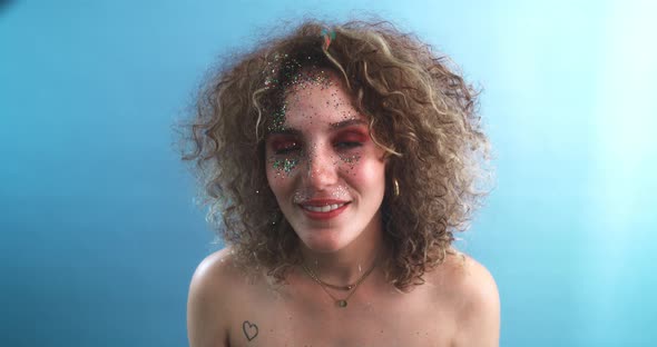Curly girl smiling and looking at the camera with her face full of glitter alt
