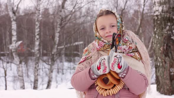 Cute girl in a traditional Russian headscarf and mittens playing on spoons on winter forest backgrou alt