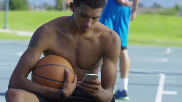 Teen basketball player using cell phone at outdoor court