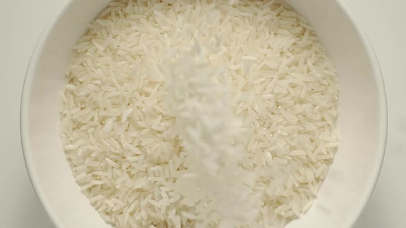 White Rice Grains Falling Into A White Bowl