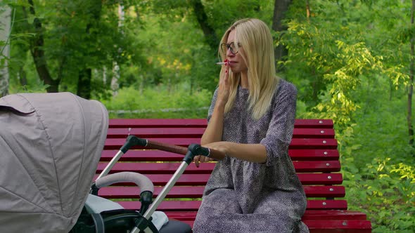 Young Mother Stroller Is Sitting Park Bench Smoking alt