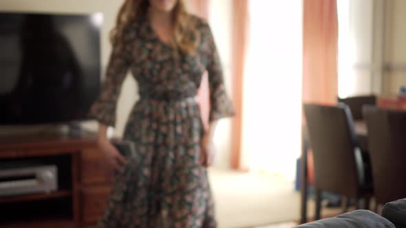 Lady walks towards and sits down on sofa in living room to use smart phone alt