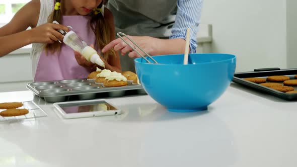 Mother helping girl to decorate cupcake with cream alt