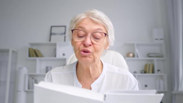 Emotional grey haired grandmother with glasses reads fairytale book alt