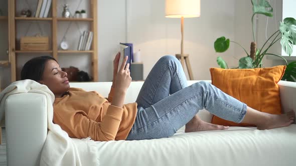 African Woman is Reading Book on Sofa in Bright Room Spbd alt