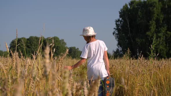 Girl with Suitcase Walking in a Wheat Field alt