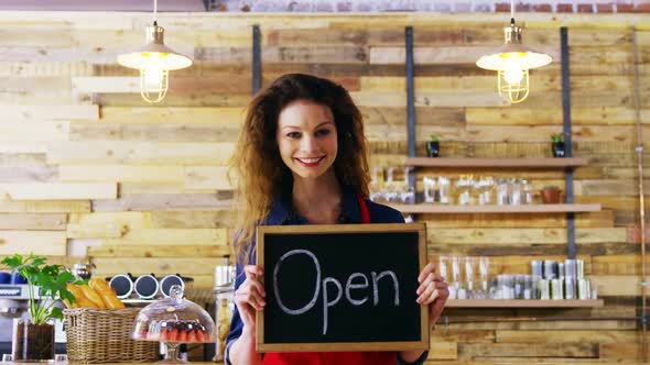 Portrait of smiling waitresses holding open sign board alt