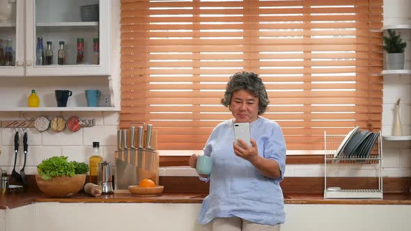 Portrait senior Asian woman using smartphone happy and smiling in the kitchen at home.