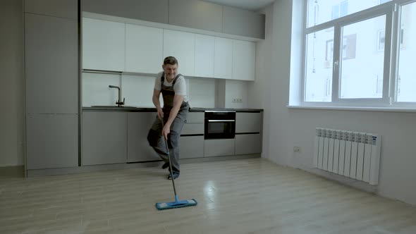 A Cheerful Worker in Uniform Washes the Floor in a New Apartment alt