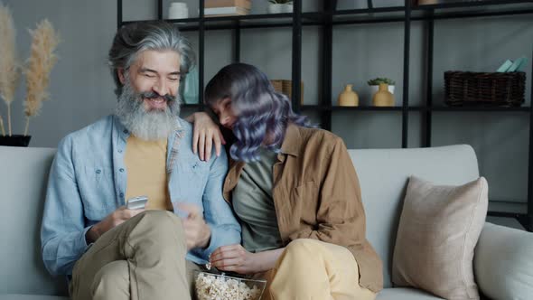 Happy Couple Watching TV Talking and Laughing Eating Popcorn in Living Room alt