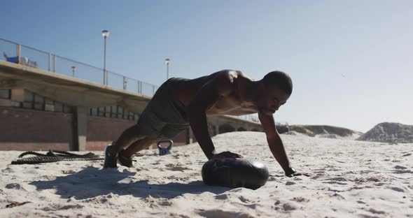 Focused african american man doing press ups on ball, exercising outdoors on beach alt