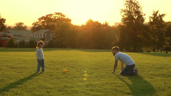 Little Child and Father Play to Football in Summer Park at Sunset