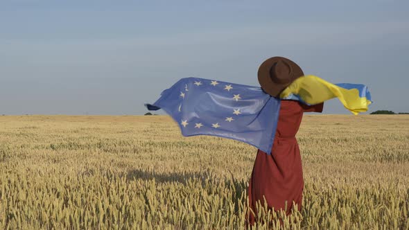 Girl with Ukraine and EU flags in wheat field and blue sky on background