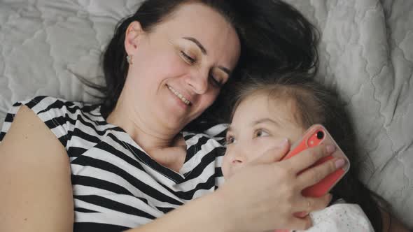 A Woman and Her Daughter are Lying on the Bed Together Hugging and Talking on the Phone with Their