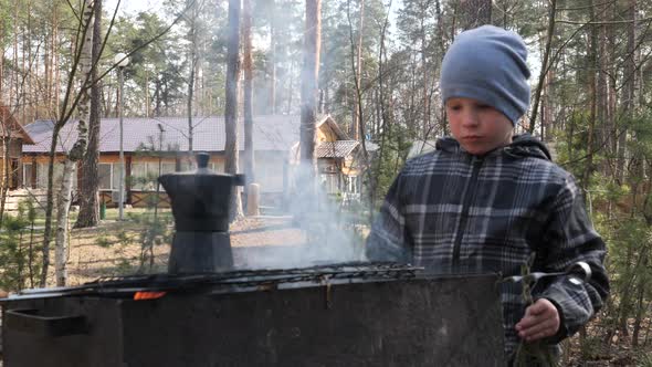 Boy cooks food on the fire in the grill. Country rest.