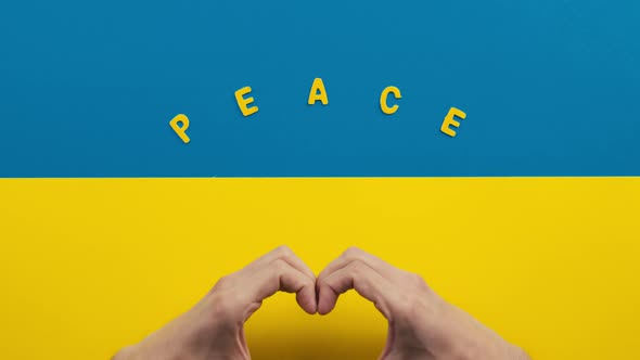 Hands Make Heart Symbol on Ukraine Flag with Peace Inscription alt
