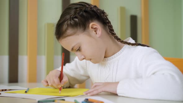 Closeup Side View of Pretty Concentrated Girl Painting with Pencil Sitting at Desk alt