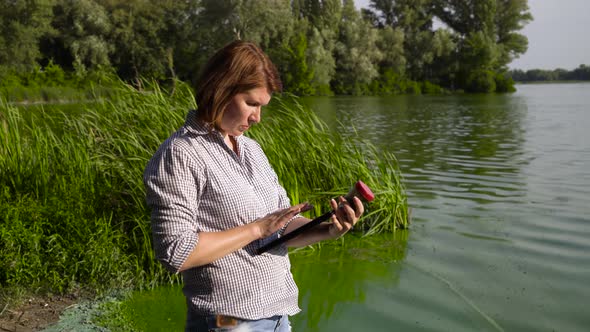 Adult Woman Ecologist Examines Sample of Green Algae and Enters Data on Tablet alt