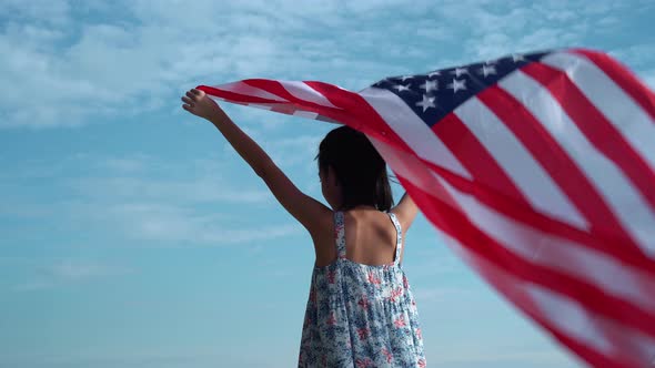 Happy beautiful girl holding USA flag, woman raise United States of America flag on sunny sky