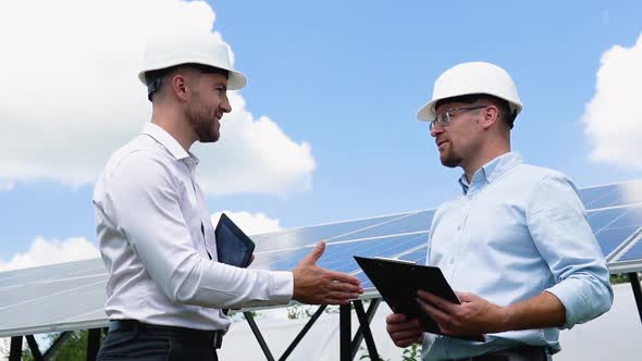 Two Male Engineer Wearing Safety Vest Handshake with Solar Panels Background alt