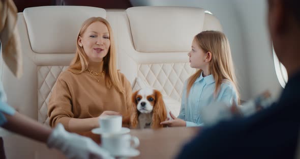 Flight Attendant Serving Coffee for Rich Couple Flying First Class with Daughter and Dog alt