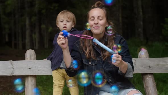 Positive Young woman with her sons playing with soap bubbles and enjoying vacation in the park. alt