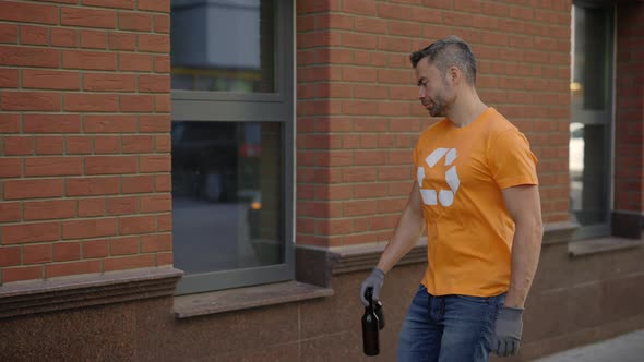 Male Volunteer is Going to the Sorting Bin Holding Two Glass Bottles and Sorting Them Wearing alt