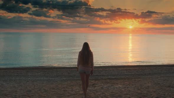 Woman with Long Hair Walking To the Sea and Raising Her Hands Up alt