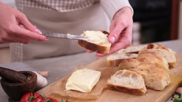 Woman Smearing Soft Butter on Slice of Baguette Bread By Knife at Domestic Kitchen alt