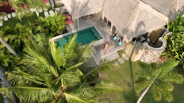 Girl enjoying good weather in luxury villa hotel with private pool surrounded by palm trees.Aerial f alt
