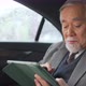 4K Senior businessman sitting on car backseat and working business plan on digital tablet