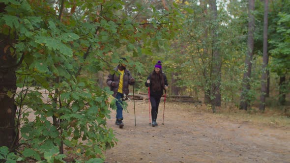 Multiethnic Couple with Trekking Poles Hiking in Wood alt