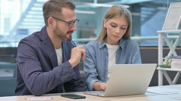 Businessman and Businesswoman Having Discussion on Laptop in Office alt