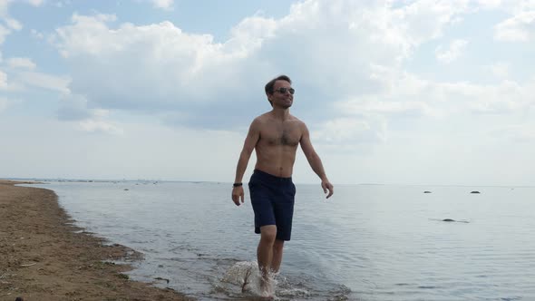 Shirtless Man Showing OK Sign While Walks Along Seashore