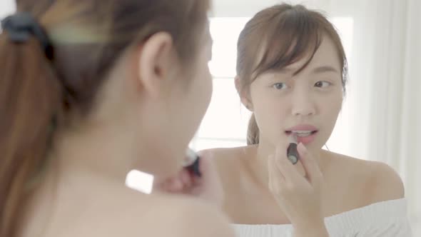 Beauty of young asian woman at the mirror applying and looking a makeup lipstick. alt