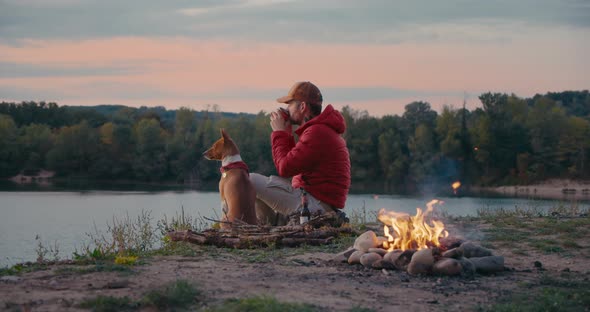 Man and Pet Dog Rest Next To Campfire on Hike Trip