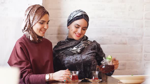Two Young Beautiful Muslim Business Women in Hijab Drinking Tea in Cafe alt