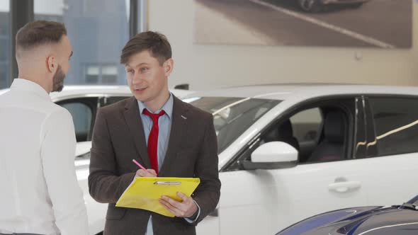 Mature Salesman Helping Male Customer Choosing Automobile to Buy alt