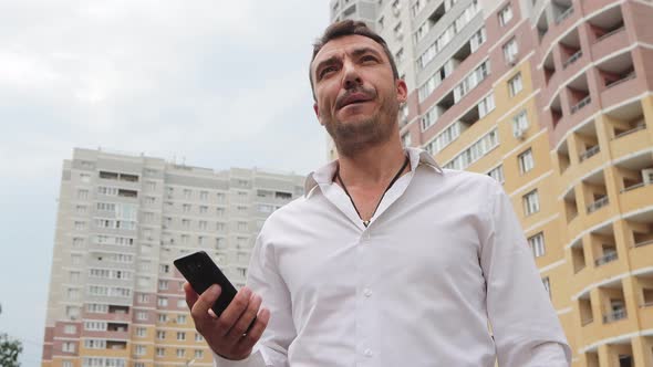 Young Businessman Emotionally Explains with a Phone in His Hand alt