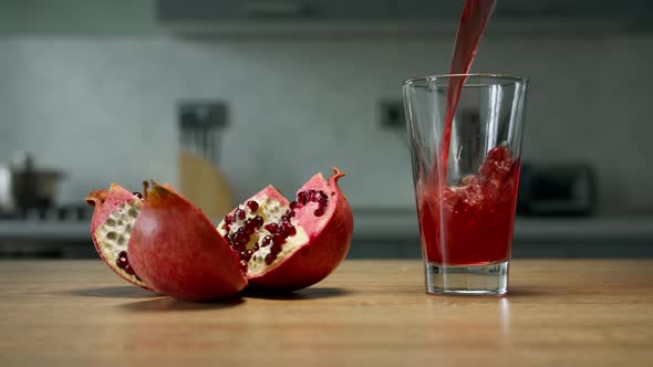 Pomegranate juice is poured into glass on wooden surface with pomegranate divided in parts