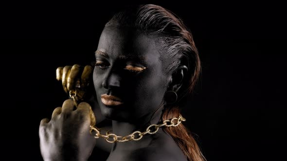 Closeup of a Woman with Black and Gold Paint and a Gold Chain Posing in Studio alt