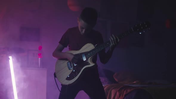 Teenager Playing Guitar Near Bed at Night alt