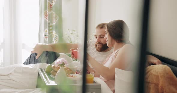 Happy Couple Lying on Bed,laughing and Watching Funny Photos on Smartphone. Good Looking Man and alt