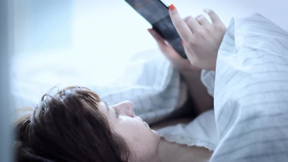 Cinematic Sleepy Brunette Woman Lies on the Bed and Uses the Phone in the Morning Read Some