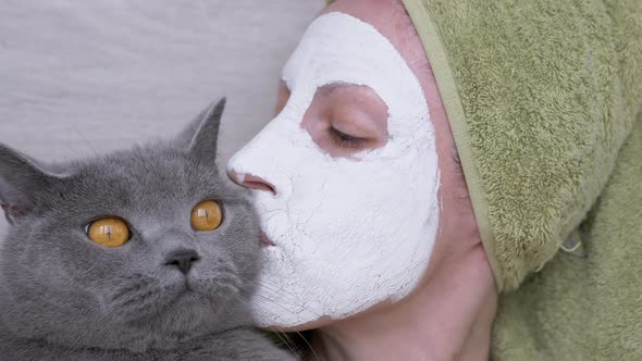 Woman in a Mask of White Clay on Face Holds a British Cat in Arms alt