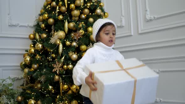 Boy Child in a White Sweater and Hat Stands at the Christmas Tree alt