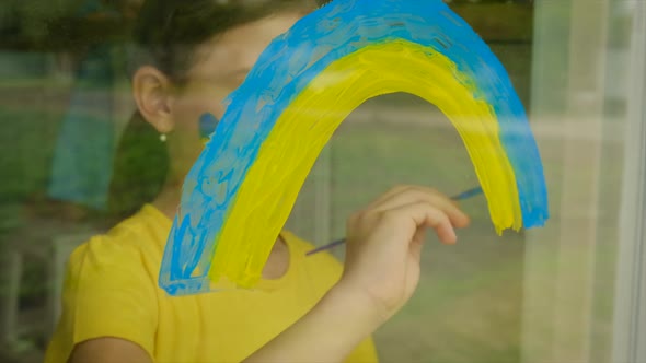 A Child Draws a Ukrainian Rainbow on the Window of the House alt