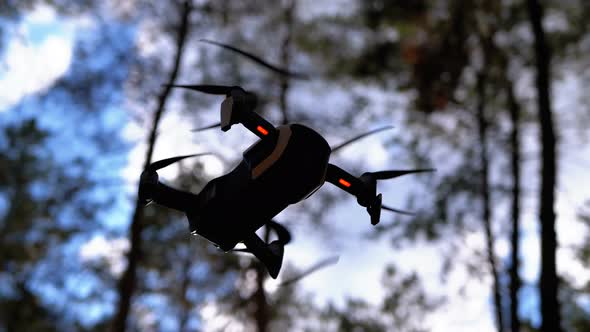 Drone with a Camera Hovers in the Air. Flies Above the Ground in the Forest. Slow Motion alt